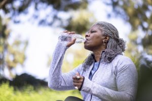Senior black woman working out drinking water and staying healthy outdoors