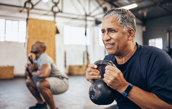 senior man exercising with personal trainer at the gym. Doing squats with kettlebell for strength.