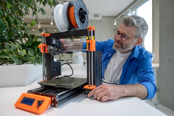 Modern 3D printer equipment and mature man working with it in office.