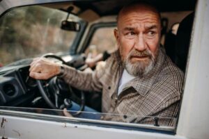 An older man backs up his car